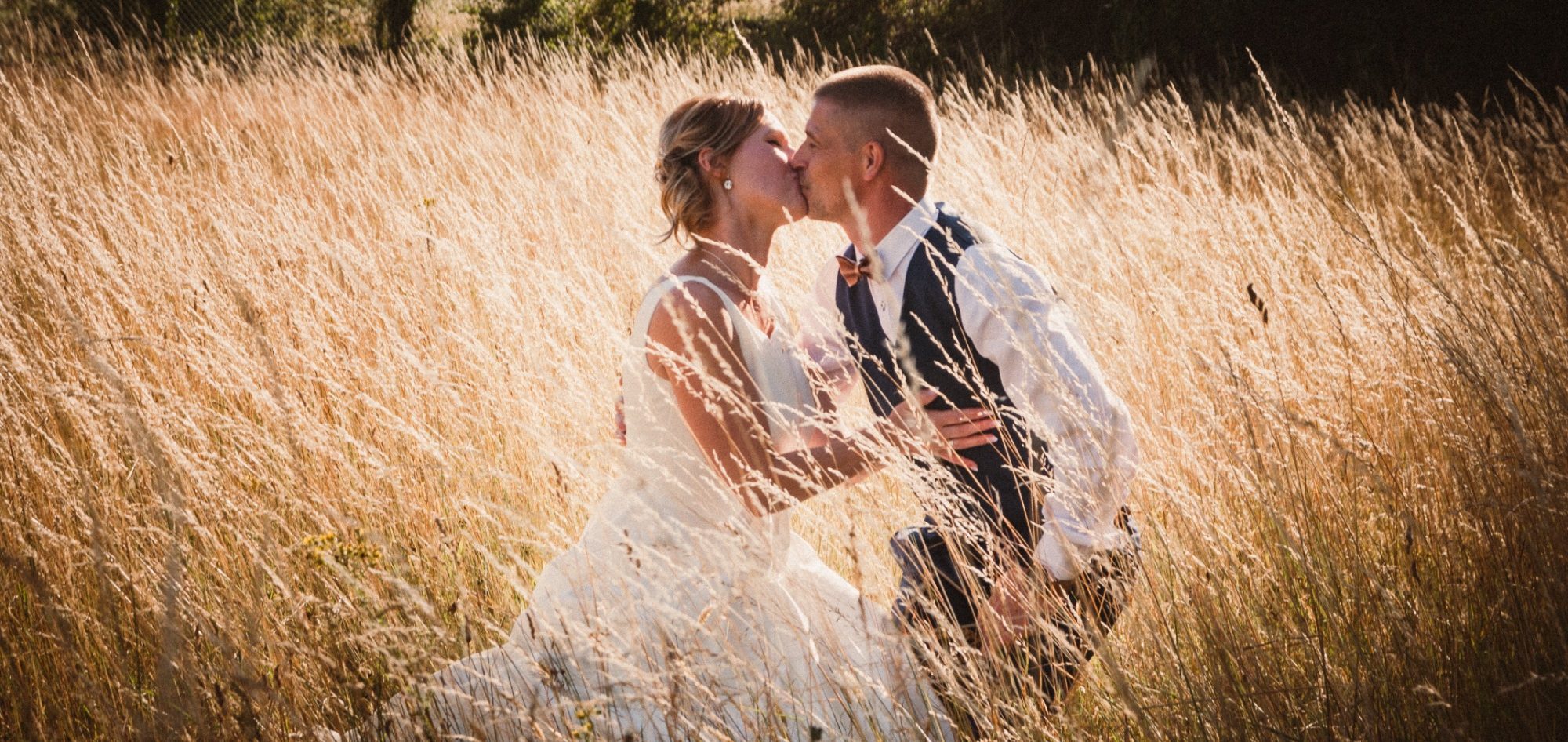 Un couple en tenue de mariage s'embrassant dans un champ de blé.